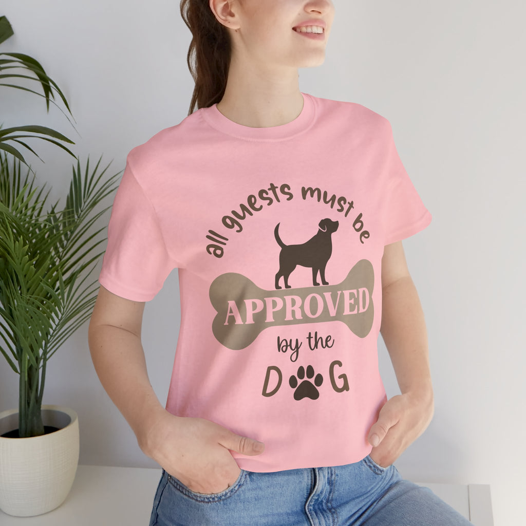 Person wearing a pink t-shirt with a dog-themed design, sitting indoors next to a plant.