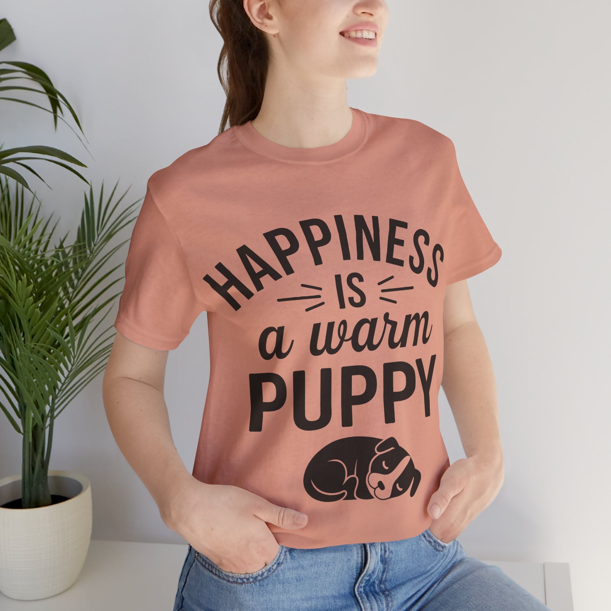 Person wearing a pink t-shirt with 'Happiness is a warm puppy' text and graphic.