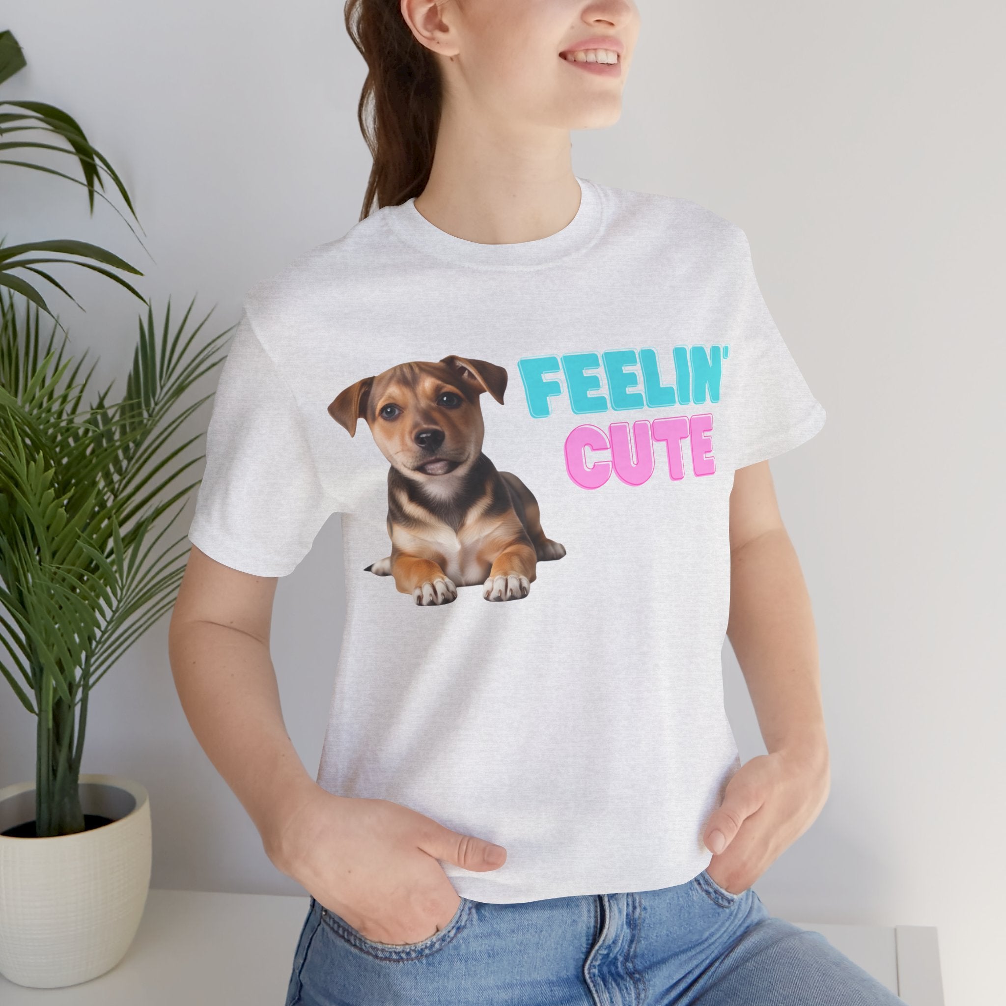 Person wearing a white t-shirt with a dog graphic and 'FEELIN' CUTE' text, standing indoors.