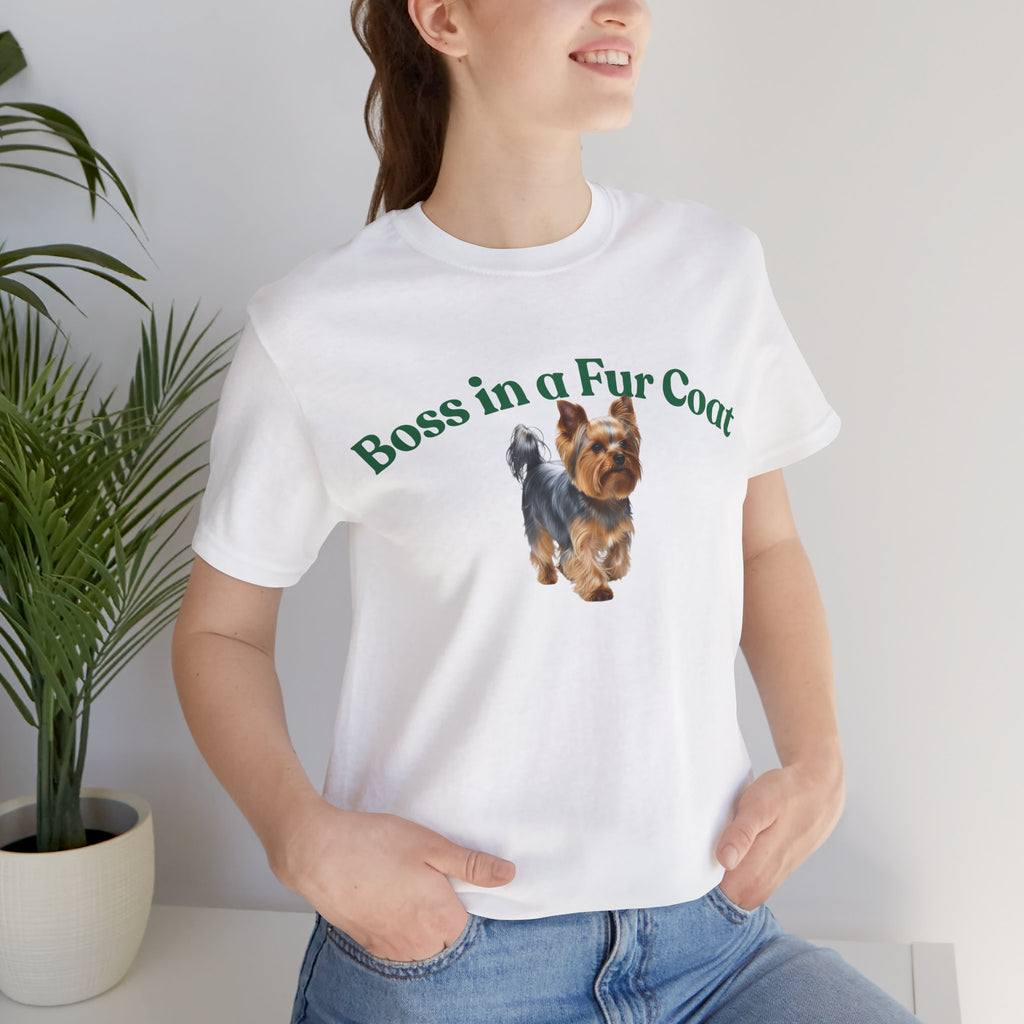 Person wearing a white t-shirt with a dog graphic and text, standing indoors next to a plant.