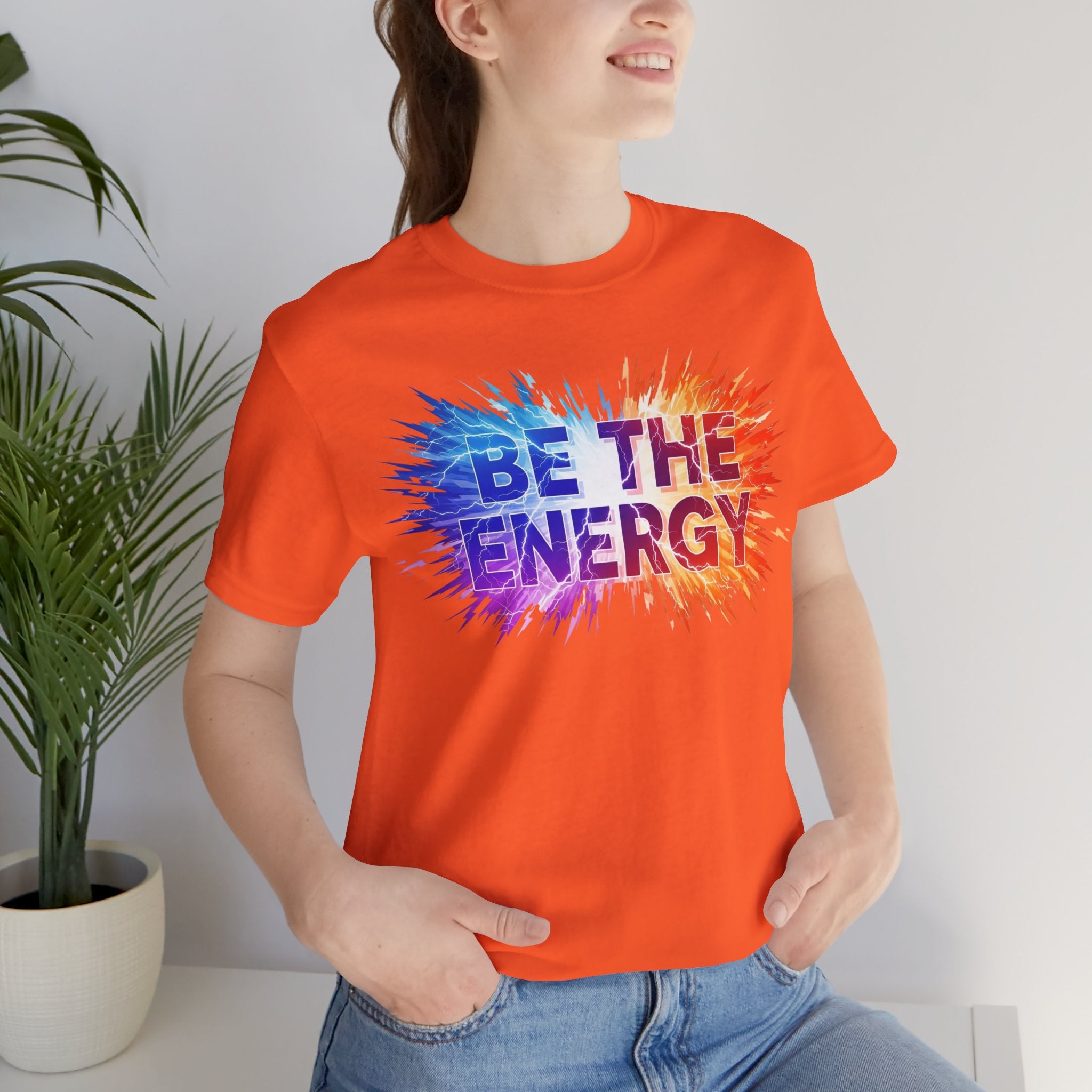 Person wearing an orange t-shirt with 'BE THE ENERGY' text, standing indoors.